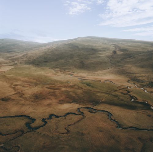 Free Aerial photograph capturing a vast, serene landscape with meandering river and distant mountains under a clear sky. Stock Photo