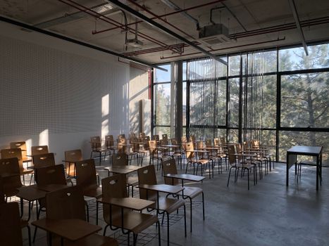 Sunlit empty classroom in Ankara, Türkiye, featuring rows of wooden chairs and desks by a large window.