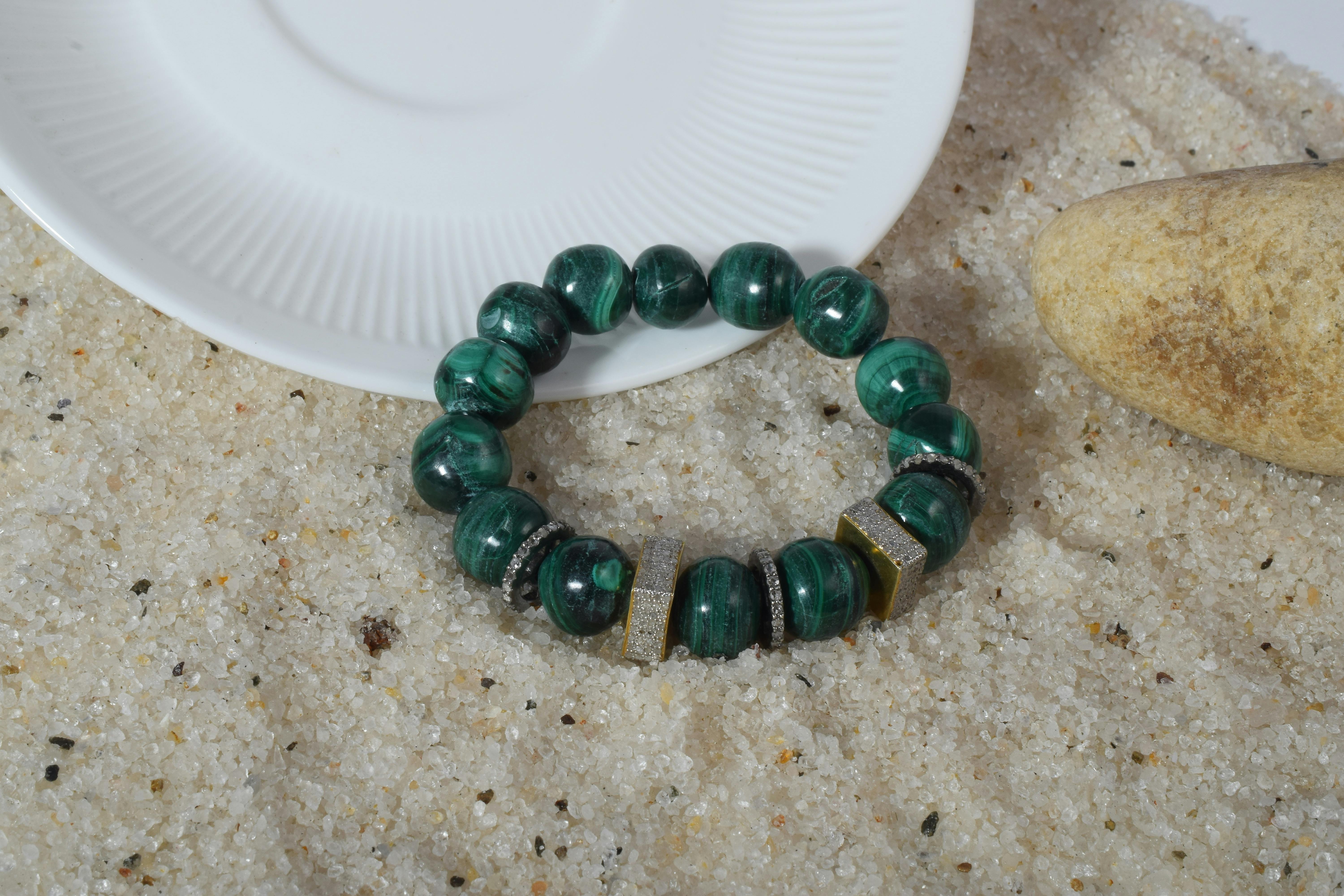Chic malachite bead bracelet on sand with plate and stone accents.