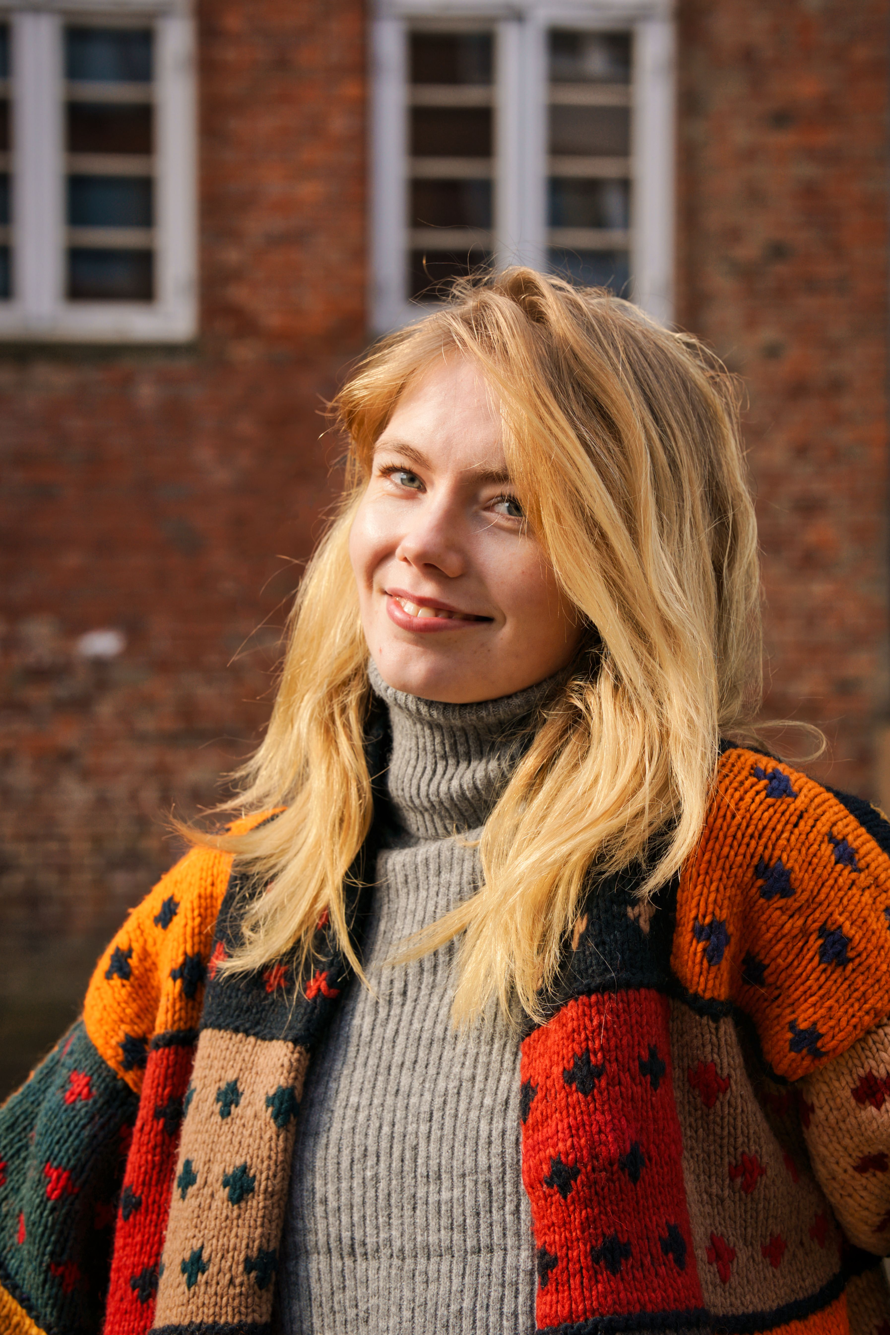A smiling blonde woman poses outdoors wearing a colorful sweater in Hamburg, Germany.