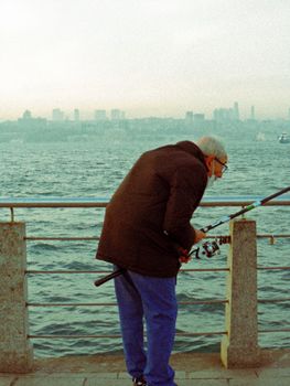 An elderly man with a fishing rod along the Bosporus in Istanbul, adding to the urban cityscape.