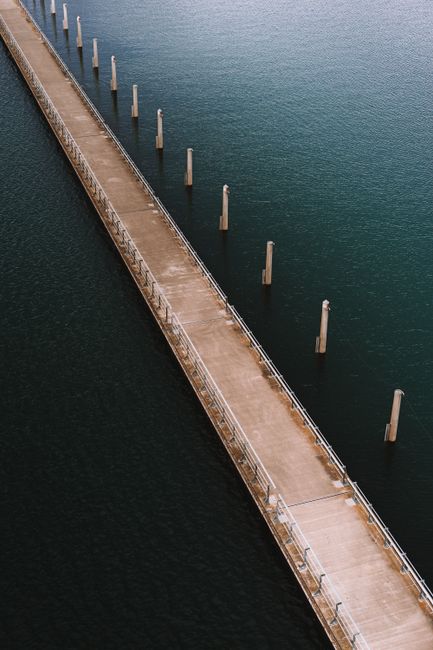 Bird's-eye view of a long pier extending into the ocean, surrounded by calm, turquoise waters.