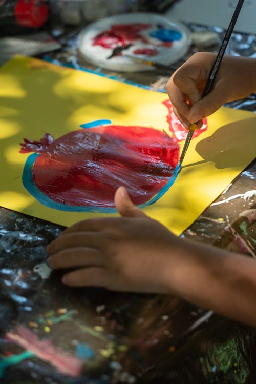 A child is painting a red apple on a piece of paper