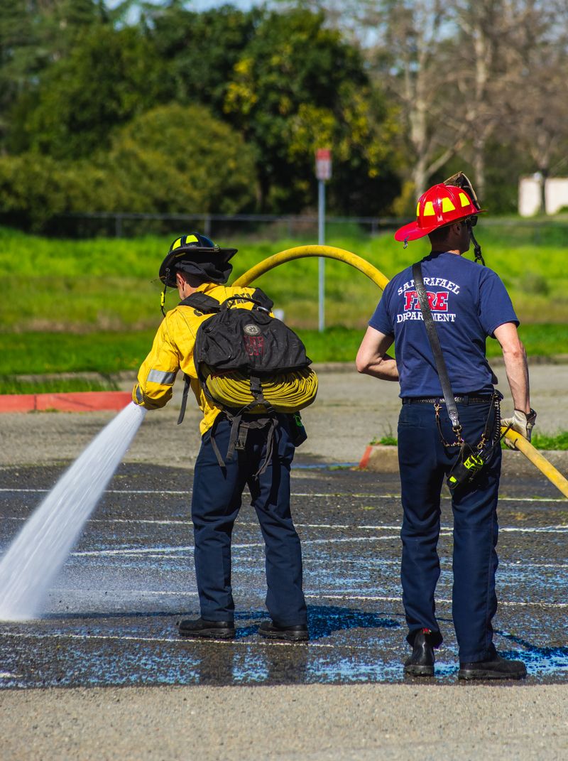 Two firefighters actively using a water hose outdoors, ensuring safety in emergency response.