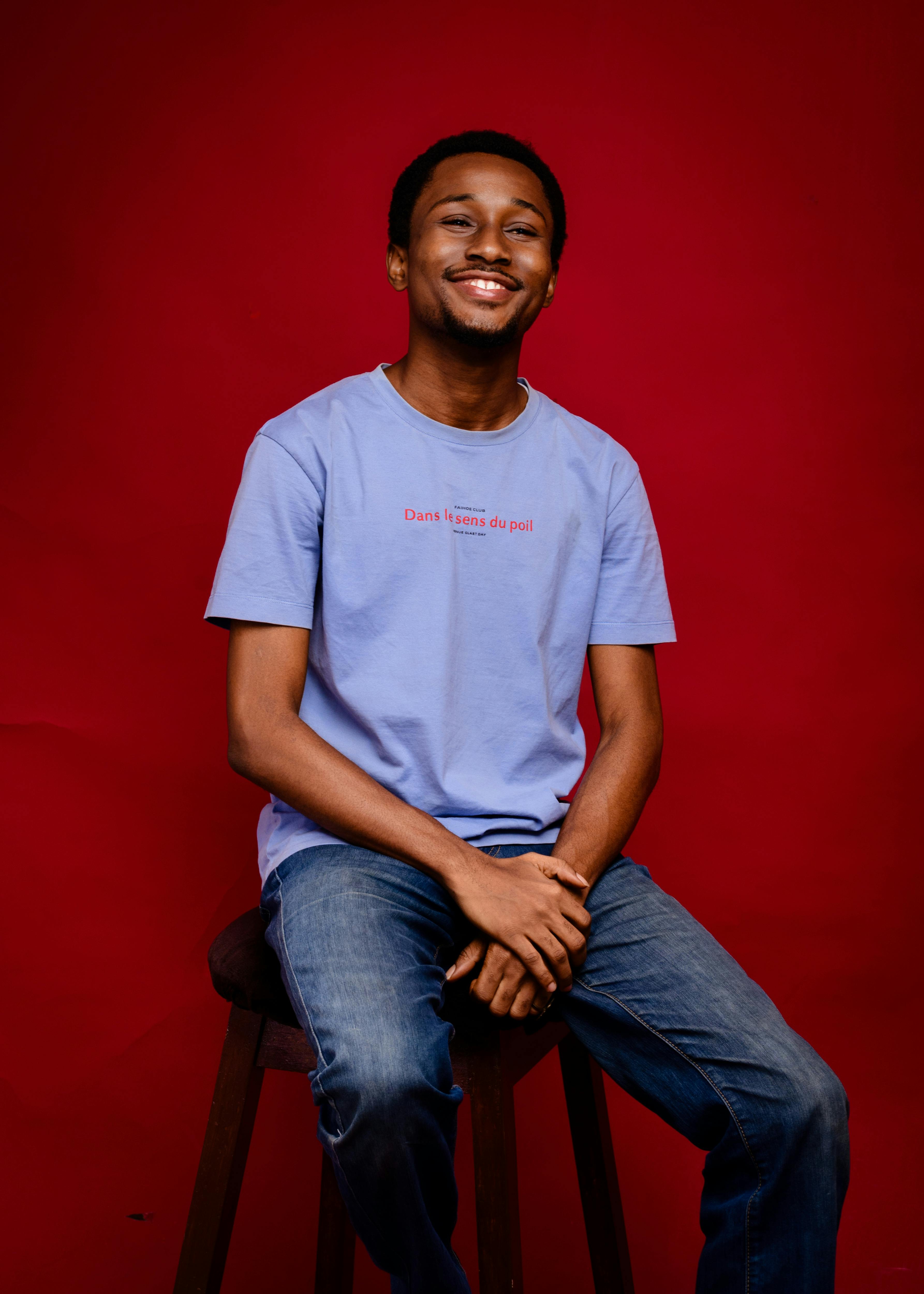 A cheerful man in casual attire smiling against a vibrant red studio background.