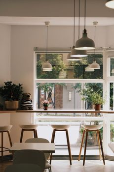 Cozy modern cafe interior with hanging lamps, stools, and large windows offering natural light.