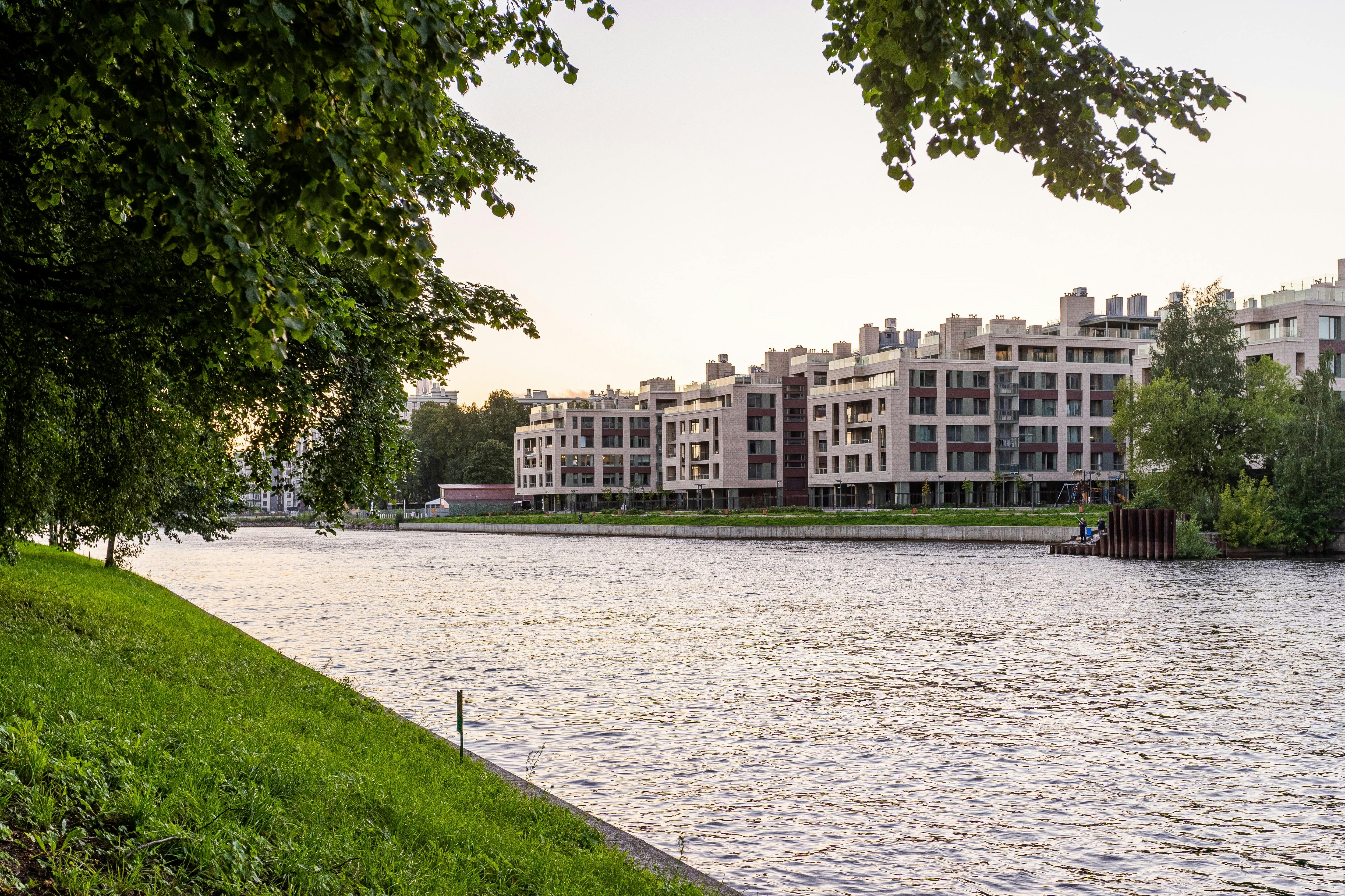 Contemporary apartments along a tranquil riverbank with lush greenery in summer.