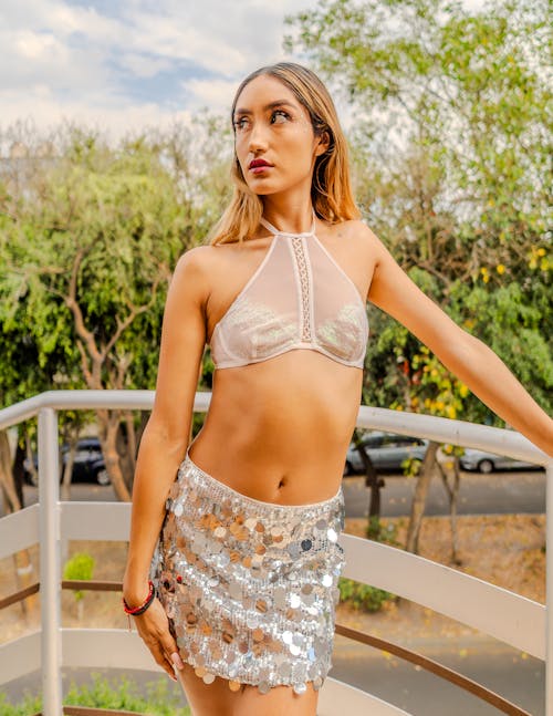 Woman in a Bra and a Sequin Skirt Standing by the Railing 