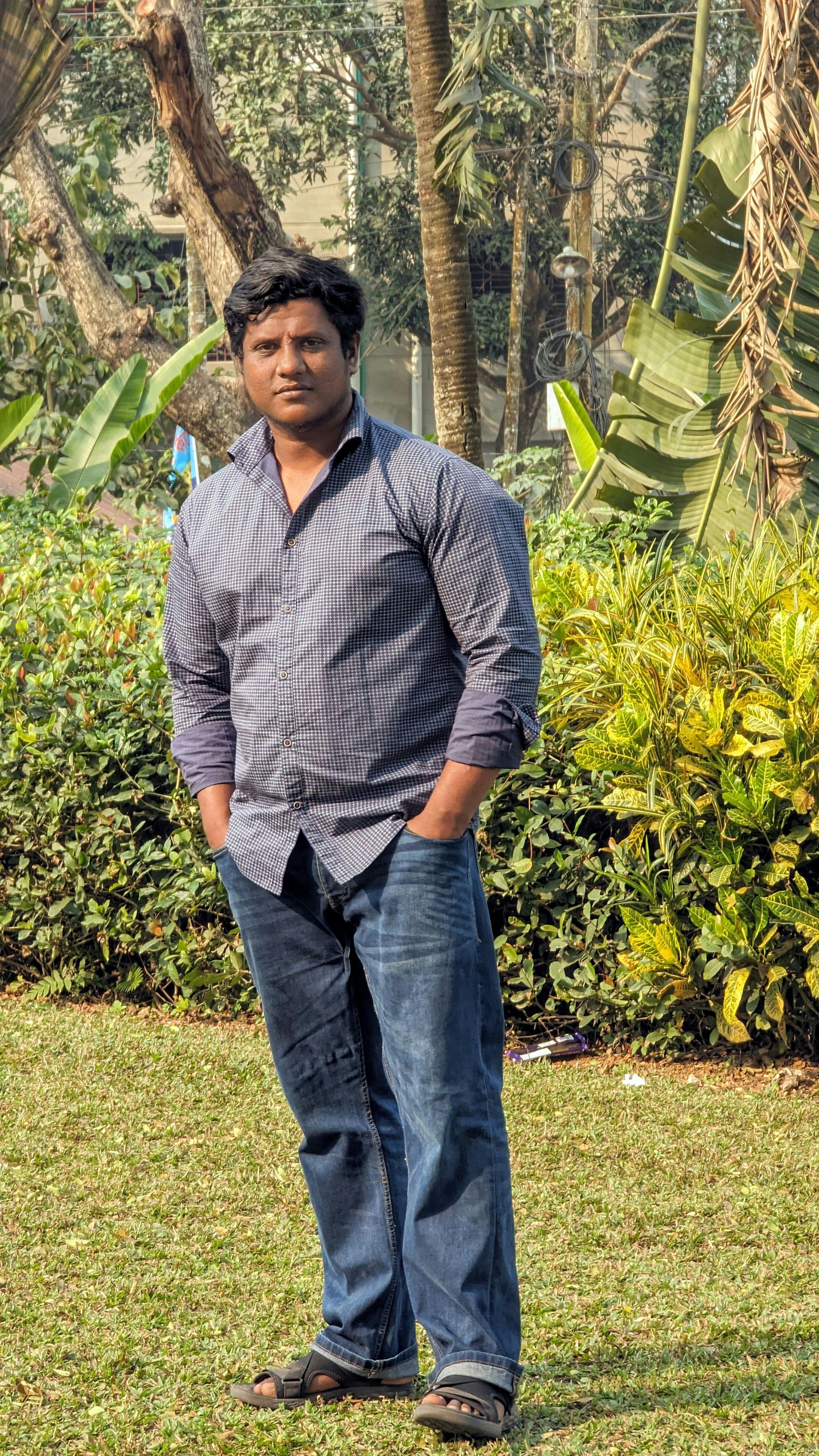 A man stands casually in a Chittagong park, showing a relaxed demeanor and casual attire.