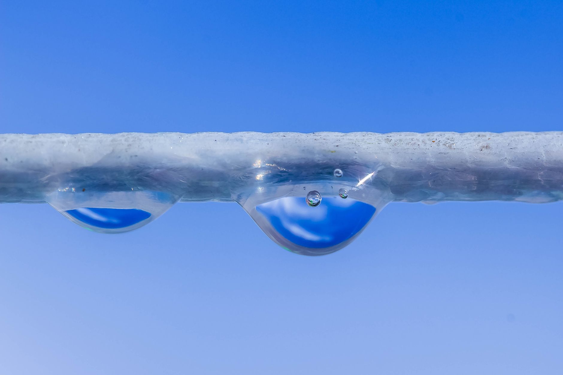 Macro shot of water droplets hanging on a rope against a clear blue sky.. macro, shot, water