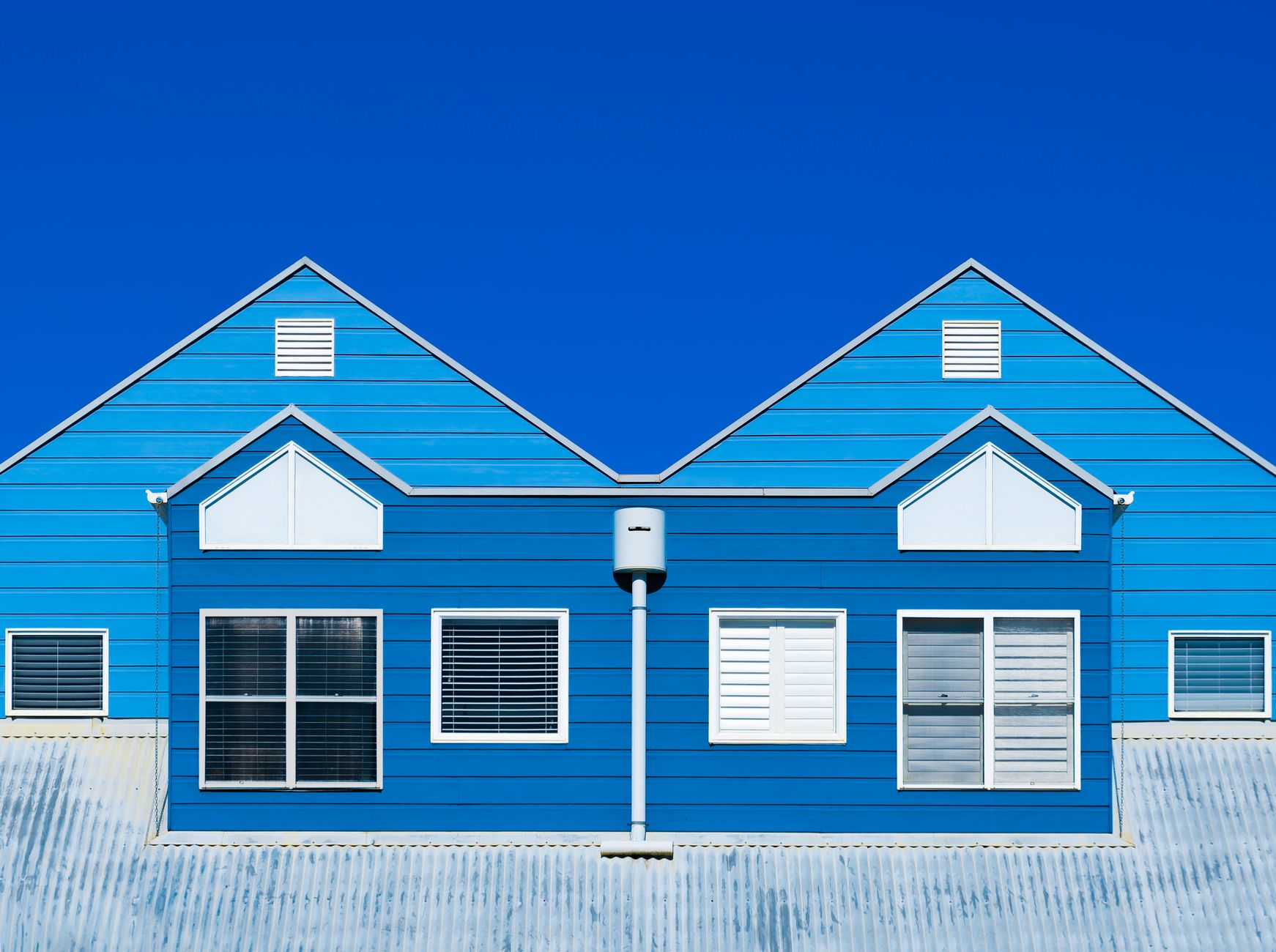 A vibrant blue house facade with windows and a clear sky, showcasing modern architecture.