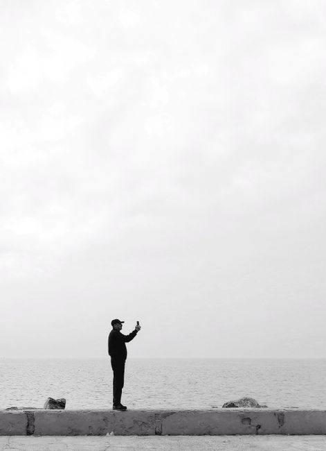 Black and white silhouette of a man taking a picture by the seaside on a promenade.