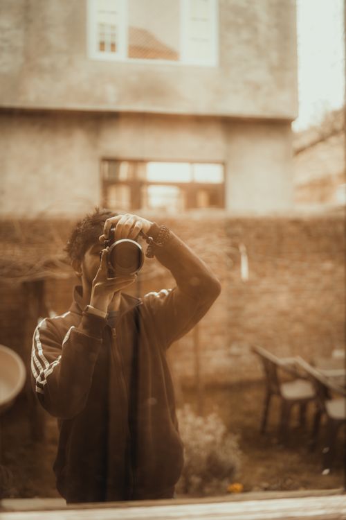 Free Sepia-toned reflection of a person taking a picture through a window in an urban area. Stock Photo
