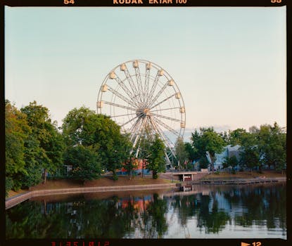 A tranquil Ferris wheel stands by a calm lake in a park, captured at dusk.