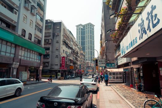 Lively city street with various buildings, cars, and pedestrians on a sunny day.
