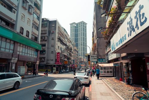 Free Lively city street with various buildings, cars, and pedestrians on a sunny day. Stock Photo
