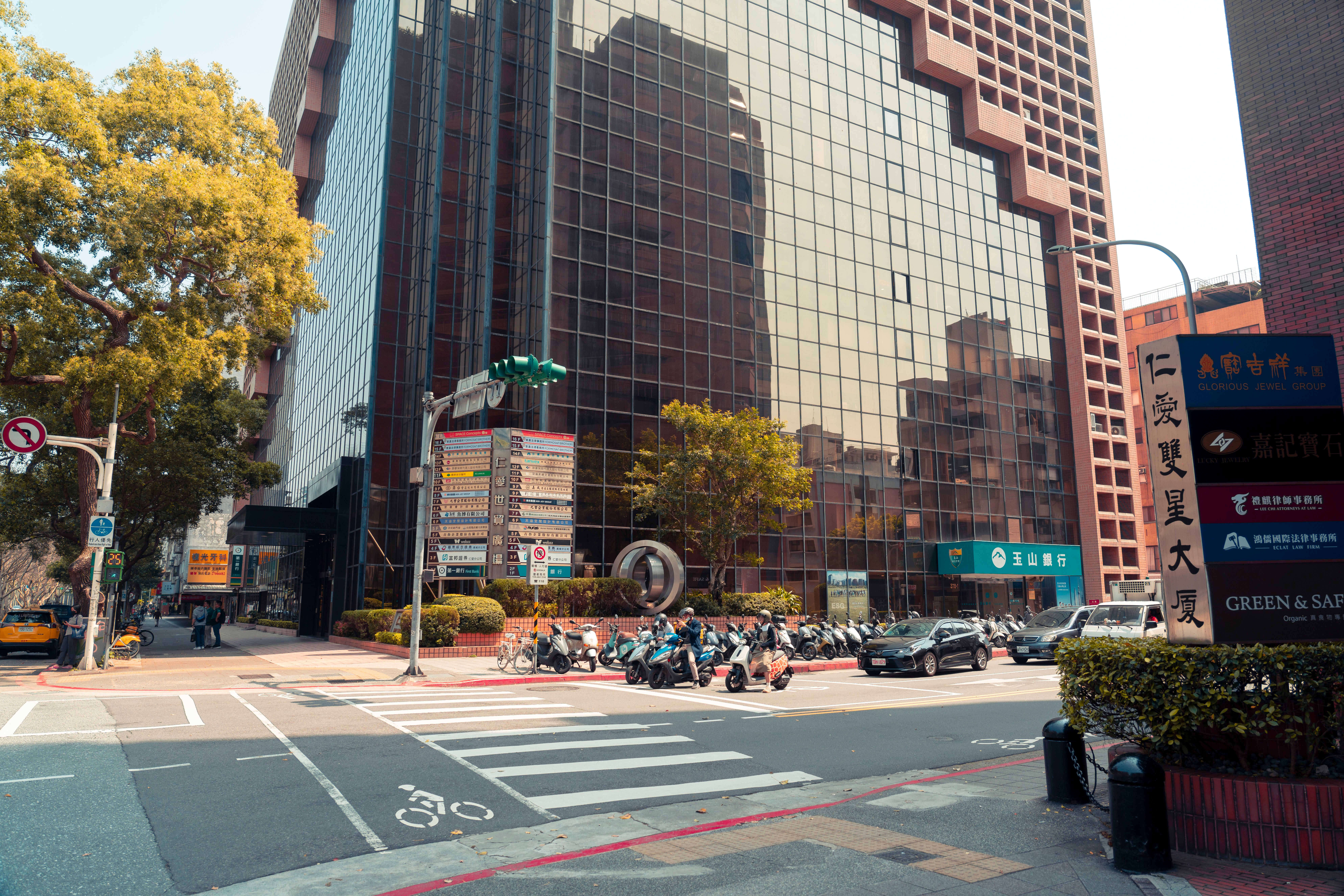 Busy city intersection with reflective skyscraper and motor scooters parked in front.