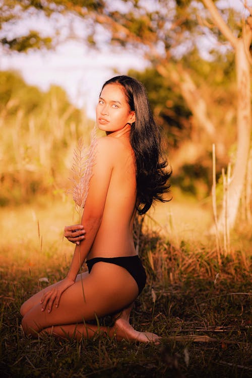 A woman in a black bikini sitting in the grass