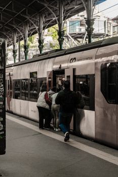 People boarding a train at a covered railway station platform in daylight.