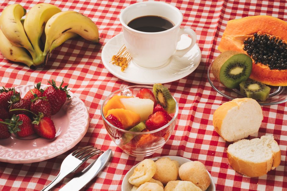 Fotomural Delicioso desayuno en la mesa con café, frutas frescas y pan sobre un mantel a cuadros.