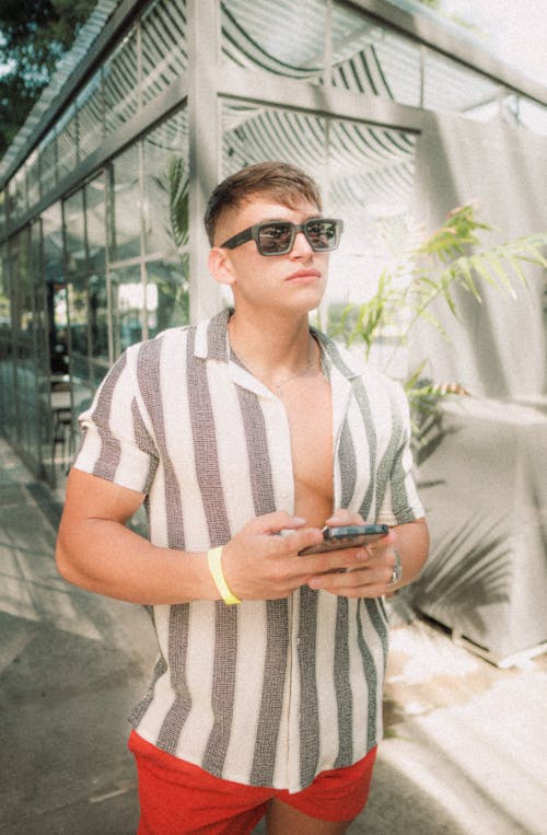 A man in sunglasses and a striped shirt is looking at his phone