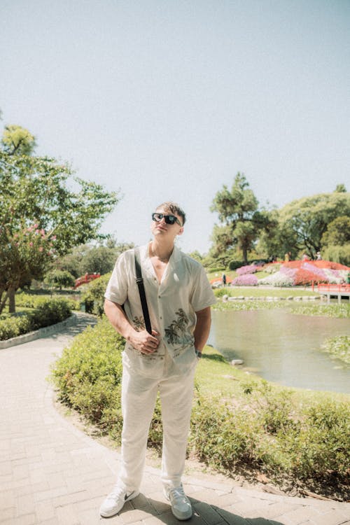 A man in white pants and sunglasses standing in front of a pond
