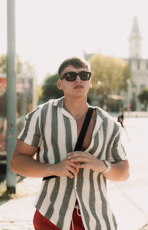 A man in sunglasses and striped shirt walking down the street