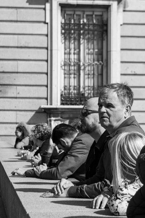 A black and white photo of people sitting on a ledge