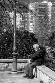 Elderly man sitting on a wall in an urban park, captured in a dramatic black and white style.