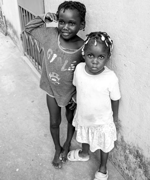 Free Charming black and white photograph of two young girls posing against a wall, showcasing innocence and joy. Stock Photo