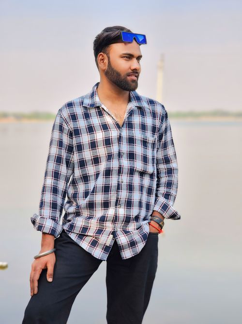 Free Casual portrait of a man in a plaid shirt, standing by a calm body of water outdoors. Stock Photo