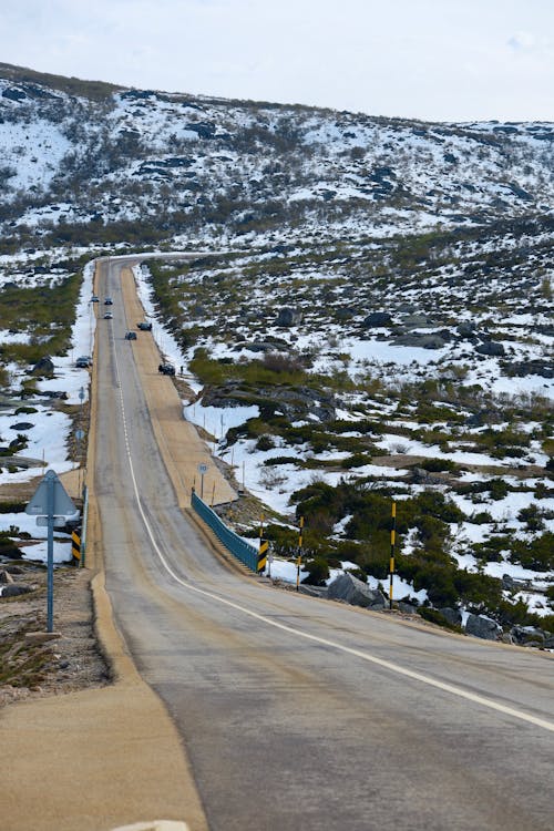 A long road with snow on the side and a mountain in the background