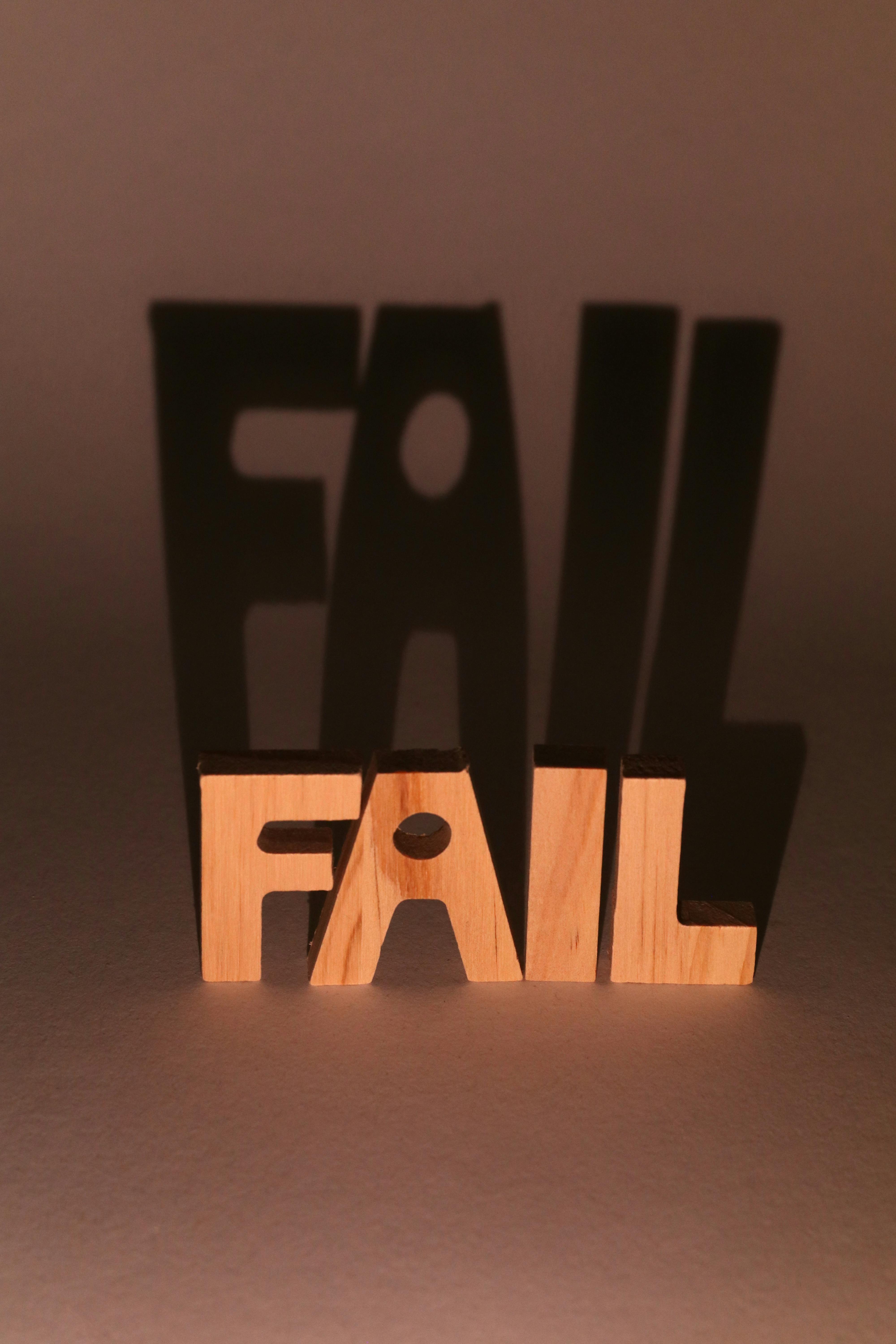 Wooden letters spelling 'FAIL' create dramatic shadows in a studio setting.