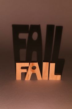 Wooden letters spelling 'FAIL' create dramatic shadows in a studio setting.