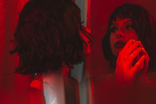 Free Artistic portrait of a woman with dramatic red lighting, capturing her reflection in a mirror. Stock Photo