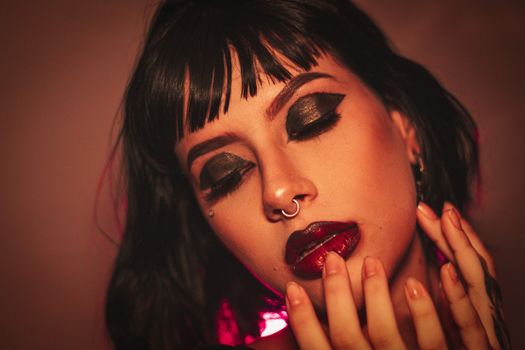 Close-up portrait of a woman with striking makeup, black hair, and nose piercing.