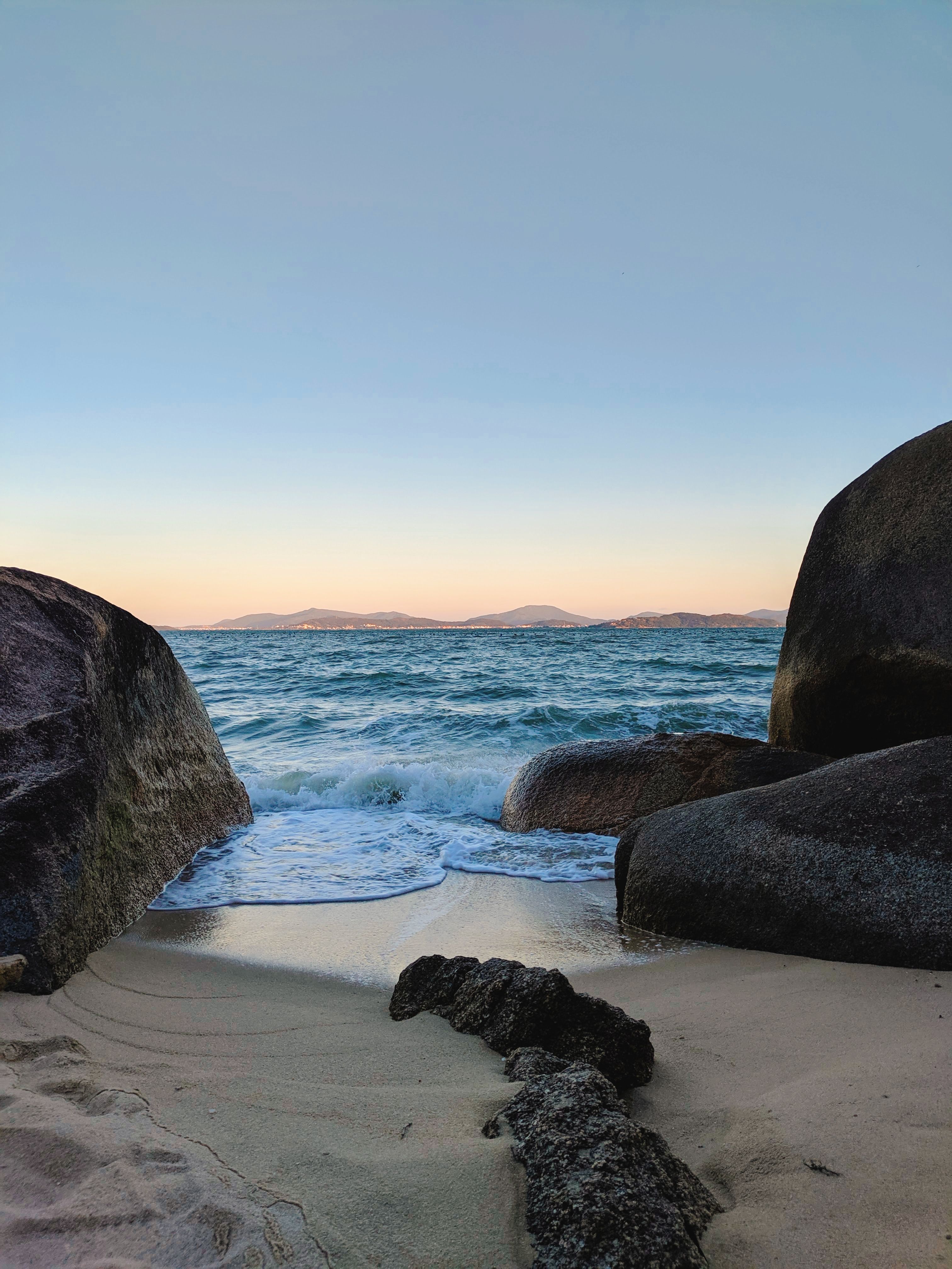 A beach with rocks and water at sunset · Free Stock Photo