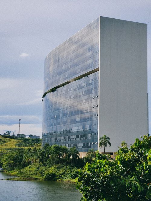 Free A modern skyscraper by a river in Belo Horizonte, Brazil, surrounded by trees. Stock Photo