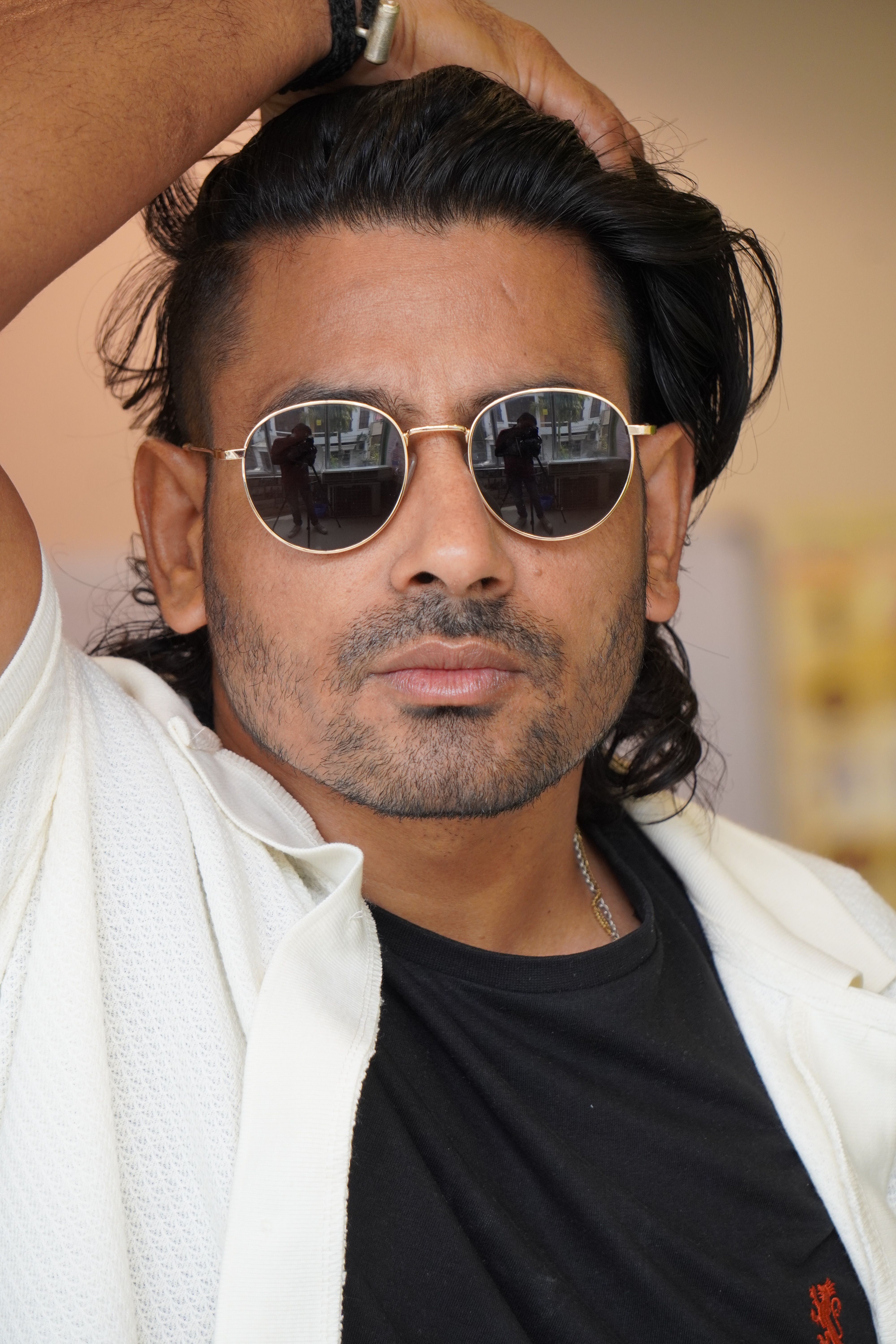 Fashionable portrait of a man with sunglasses adjusting his hair, exuding confidence and style.