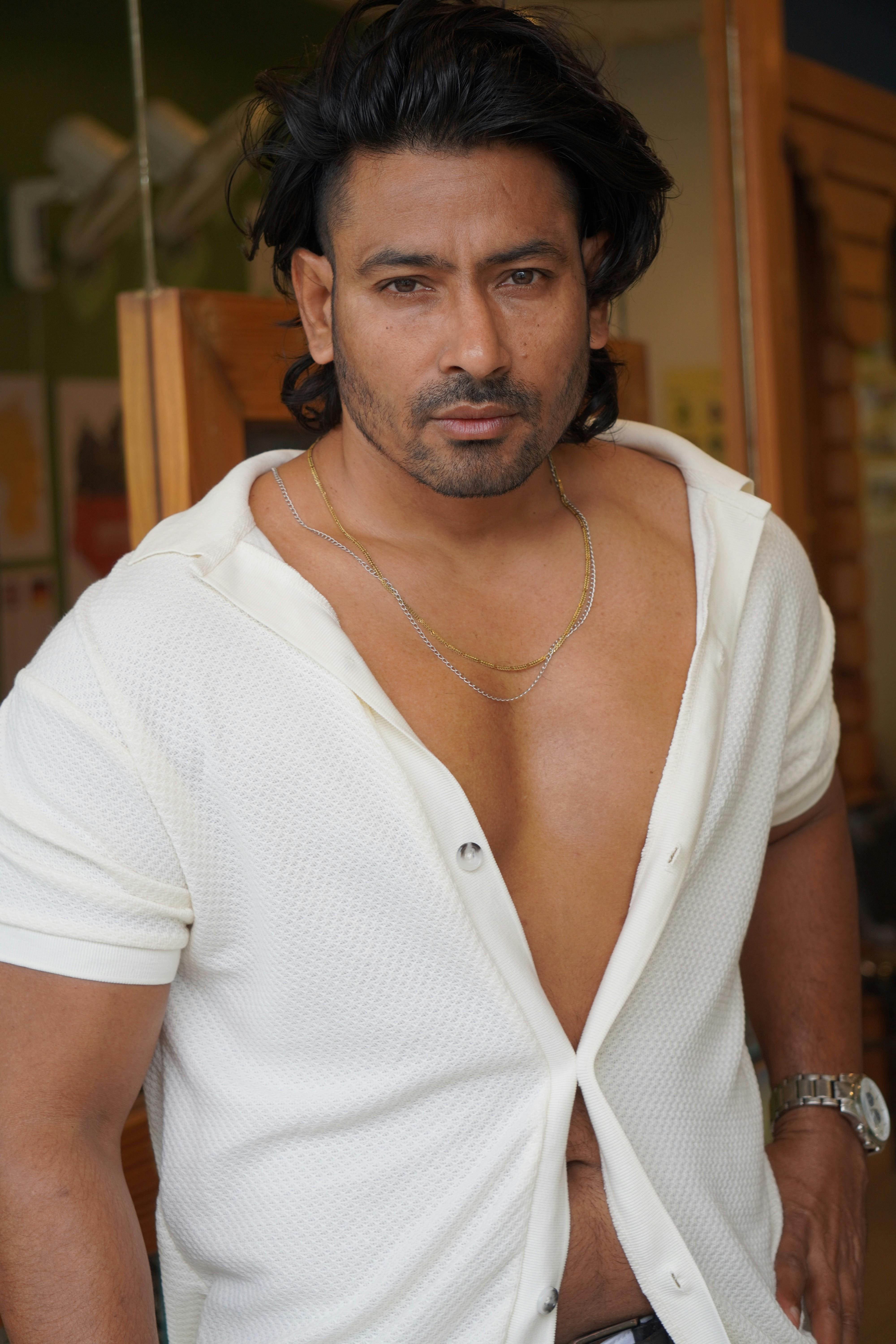 Portrait of a confident male model wearing a partially unzipped white shirt indoors.