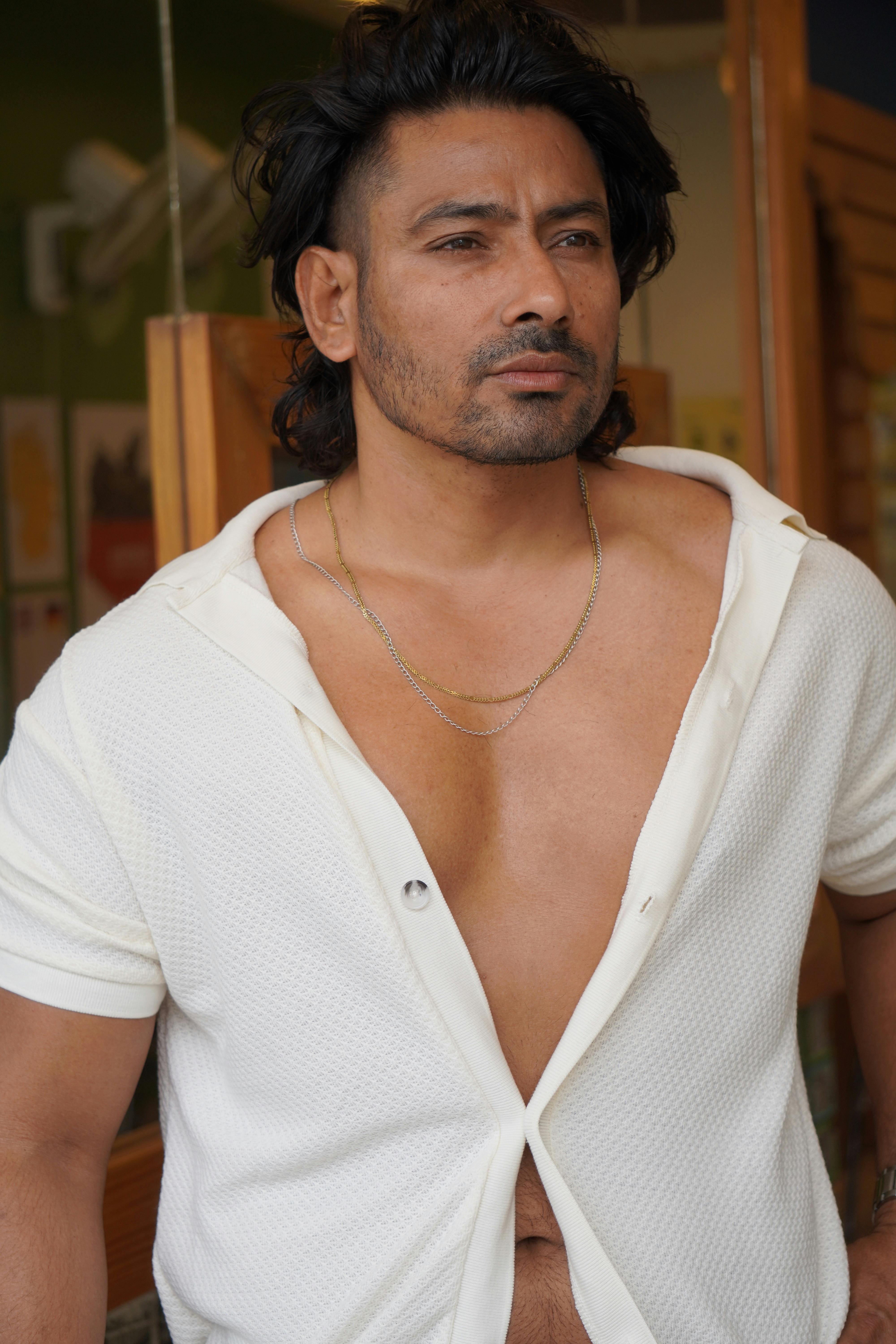 Confident man in white shirt gazing thoughtfully indoors. Stylish and relaxed scenario.
