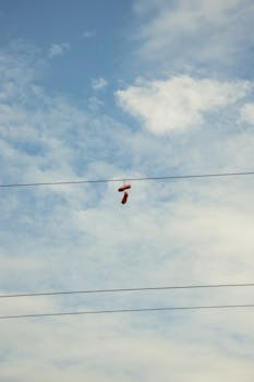 Red sneakers hanging on power lines set against a clear blue sky with clouds.