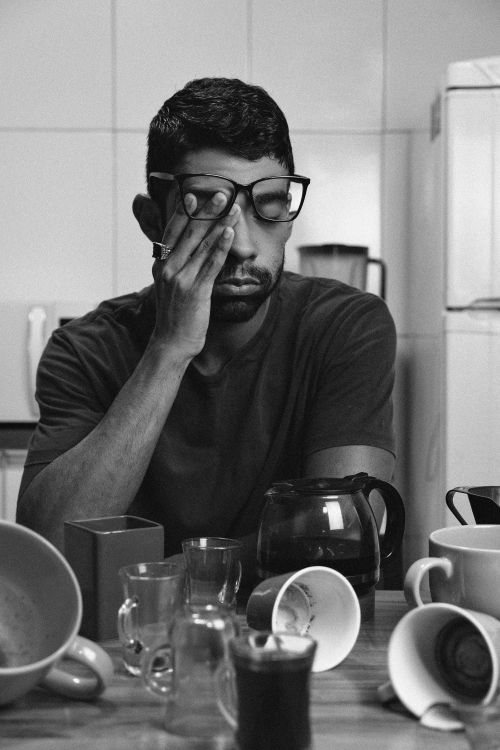 Free A tired man wearing glasses sits at a table, surrounded by empty coffee cups. Stock Photo