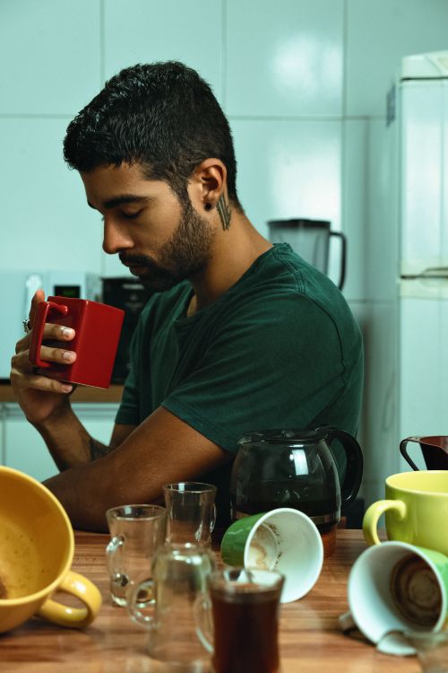 Free A man calmly sips coffee in a kitchen cluttered with empty mugs, displaying a relaxed morning routine. Stock Photo