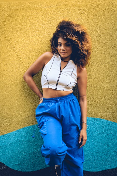 A woman with curly hair posing in front of a yellow wall