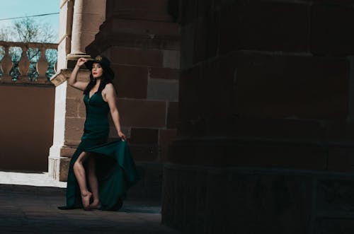 A woman in a green dress is standing on a brick wall