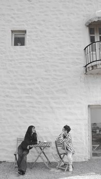 Two people engaged in a casual conversation beside a white stone building.