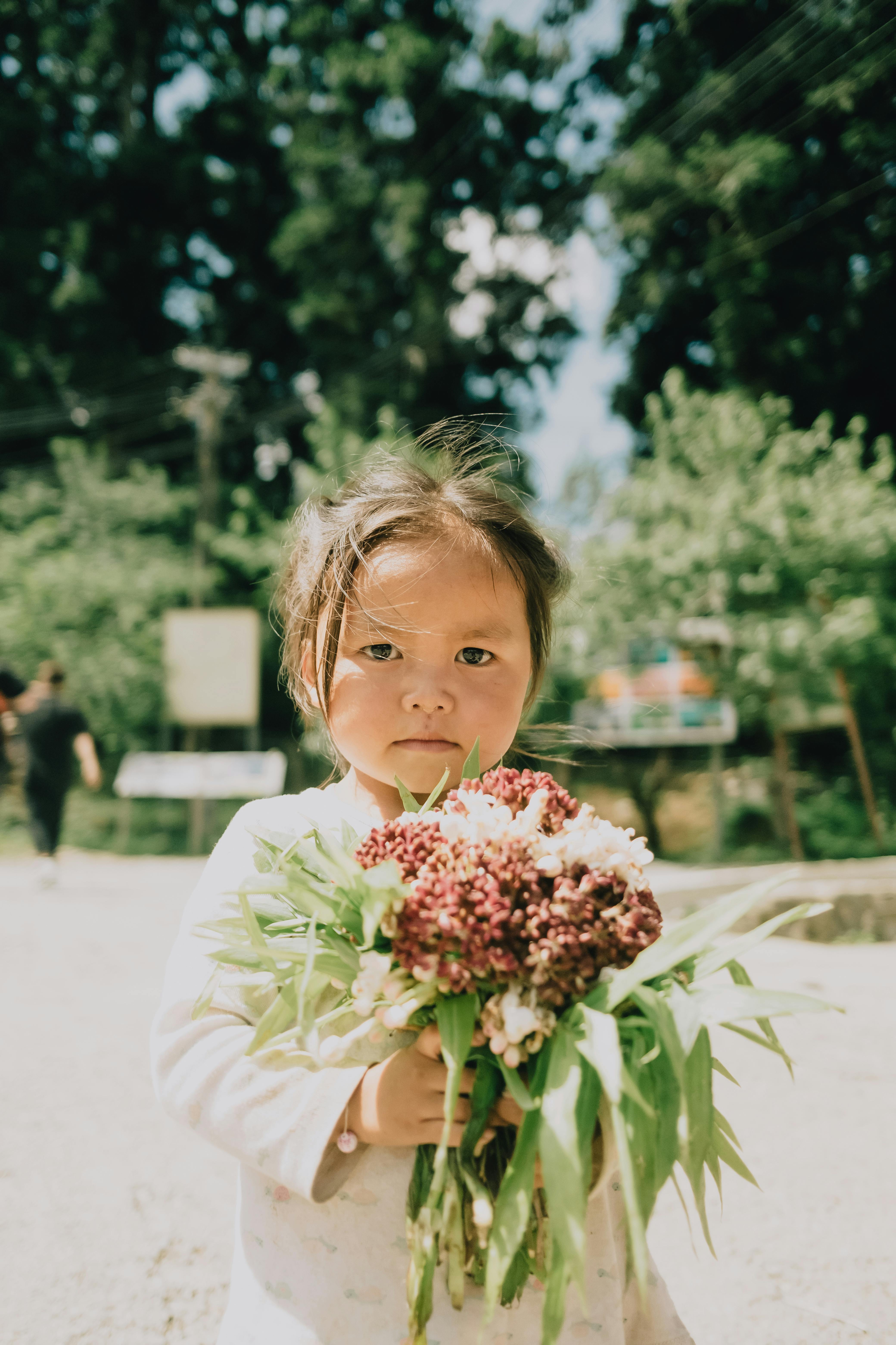Adorable child with flowers standing in a sunlit park, capturing innocence in nature.