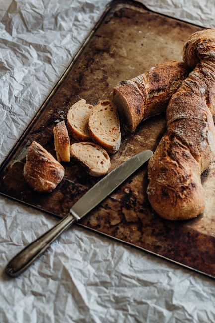 Freshly baked rustic bread loaf with slices on a textured baking tray.