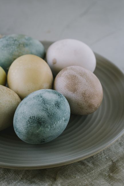 A close-up of naturally painted Easter eggs on a rustic ceramic plate, ideal for festive decorations.